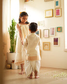A Boy wearing an off white Indian festive Kurta with golden stripes made with Handwoven cotton silk fabric woven by artisans in Maheshwar Madhya Pradesh. Sibling love. Siblings celebrating diwali. Brother and sister playdate. 