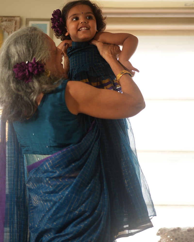 A woman wearing a deep teal blue colored cotton silk saree with golden checks handwoven by weavers in Maheshwar, Madhya Pradesh. 