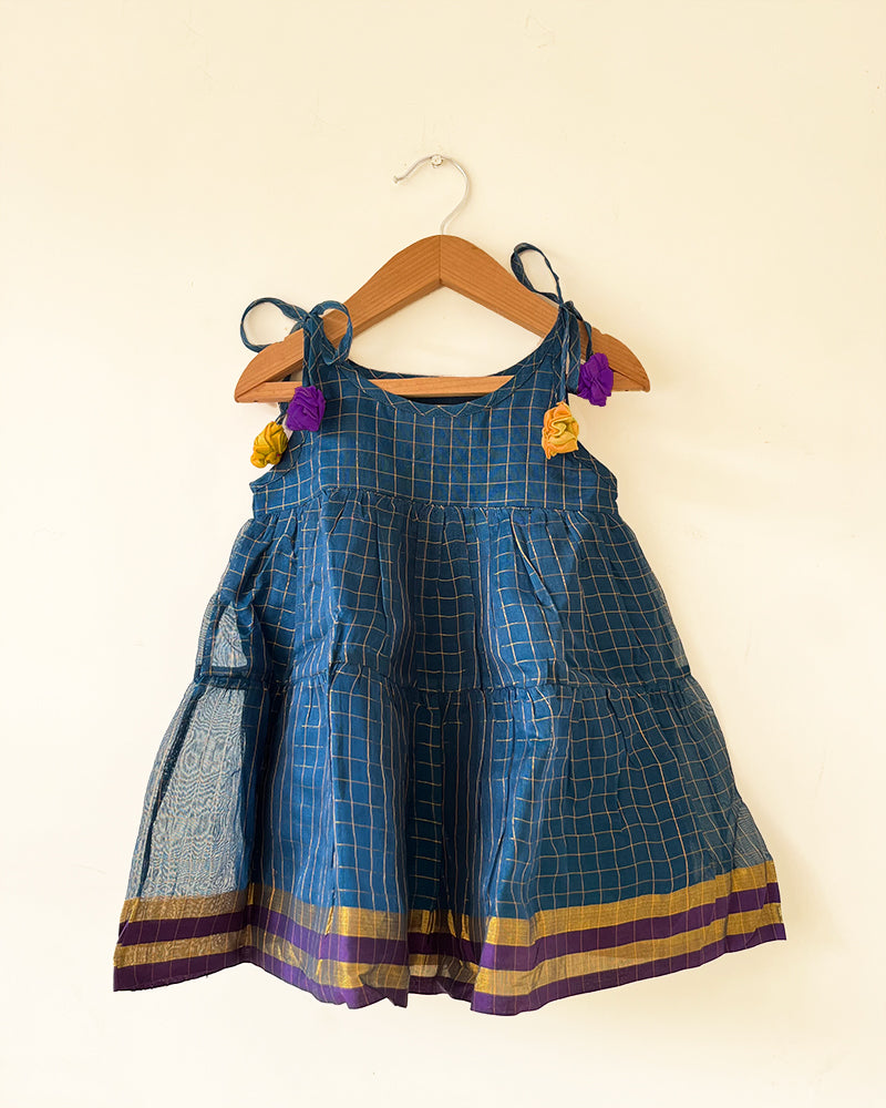 A deep teal blue sleeveless tiered dress with golden checks for infants in handwoven cotton silk by artisans in Maheshwar Madhya Pradesh. Perfect for festivities like Navratri, diwali, Dussehra, dushehra, bhai dooj. Infant wear. Baby ethnic wear. Silkwear for babies. Baby girl festive wear. 
