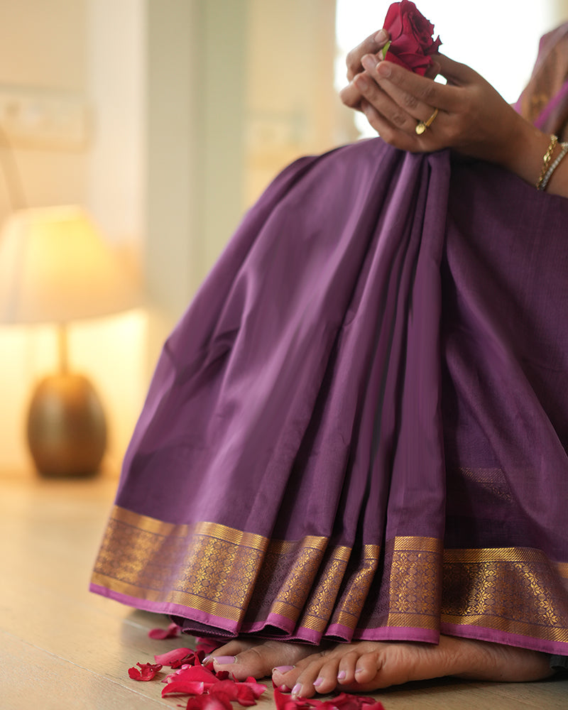 A woman wearing a deep purple wine colored cotton silk saree handwoven by weavers in Maheshwar, Madhya Pradesh. This Maheshwari Cotton silk saree is perfect for festivities like Navratri, durga pooja, Dussehra, dushehra, diwali pooja, bhai dooj and weddings. Paired with a golden blouse. Women's silk wear, silk saree for women, cotton silk saree, heavy pallu border sarees. 