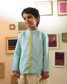 A Boy wearing a light baby blue Indian festive Kurta with golden polka dot motifs made with Handwoven cotton silk fabric woven by artisans in Maheshwar Madhya Pradesh. This kids ethnic kurta is best for upcoming festivities like kids Navratri outfit, kids durga pooja kurta, Dussehra, dushehra, ethnic dress for Diwali, bhai dooj and kids/ boys kurta for weddings. Paired with an off white dhoti/ mundu. Perfect Kids silk wear, ethnic wear for kids, festive clothing for kids.