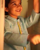 A Boy wearing a light baby blue Indian festive Kurta with golden polka dot motifs made with Handwoven cotton silk fabric woven by artisans in Maheshwar Madhya Pradesh. This kids ethnic kurta is best for upcoming festivities like kids Navratri outfit, kids durga pooja kurta, Dussehra, dushehra, ethnic dress for Diwali, bhai dooj and kids/ boys kurta for weddings. Paired with an off white dhoti/ mundu. Perfect Kids silk wear, ethnic wear for kids, festive clothing for kids.