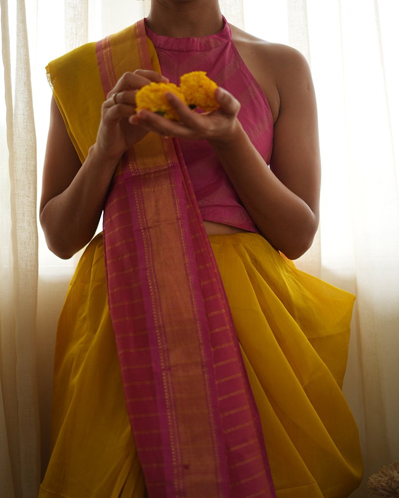 A woman wearing a bright yellow colored cotton silk saree with a pink and gold border and pallu with pink and gold stripes handwoven by weavers in Maheshwar, Madhya Pradesh. Women's silk wear, silk saree for women, cotton silk saree, heavy pallu sarees. 