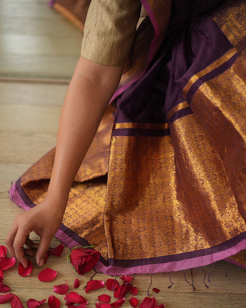 A woman wearing a deep purple wine colored cotton silk saree handwoven by weavers in Maheshwar, Madhya Pradesh. Women's silk wear, silk saree for women, cotton silk saree, heavy pallu border sarees. 