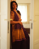 A woman wearing a deep purple wine colored cotton silk saree handwoven by weavers in Maheshwar, Madhya Pradesh. This Maheshwari Cotton silk saree is perfect for festivities like Navratri, durga pooja, Dussehra, dushehra, diwali pooja, bhai dooj and weddings. Paired with a golden blouse. Women's silk wear, silk saree for women, cotton silk saree, heavy pallu border sarees. 