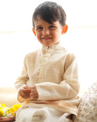 A Boy wearing an off white Indian festive Kurta with golden stripes made with Handwoven cotton silk fabric woven by artisans in Maheshwar Madhya Pradesh. Perfect Kids silk wear, ethnic wear for kids, festive clothing for kids.
