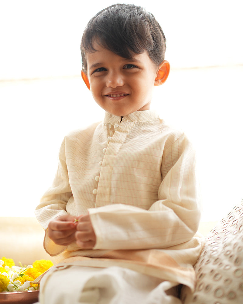 A Boy wearing an off white Indian festive Kurta with golden stripes made with Handwoven cotton silk fabric woven by artisans in Maheshwar Madhya Pradesh. Perfect Kids silk wear, ethnic wear for kids, festive clothing for kids.