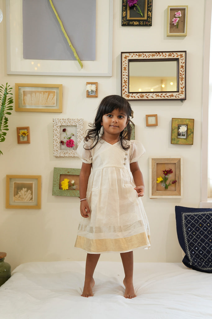 Little girl in white ethnic frock/dress with gold and silver detailing smiling for the camera