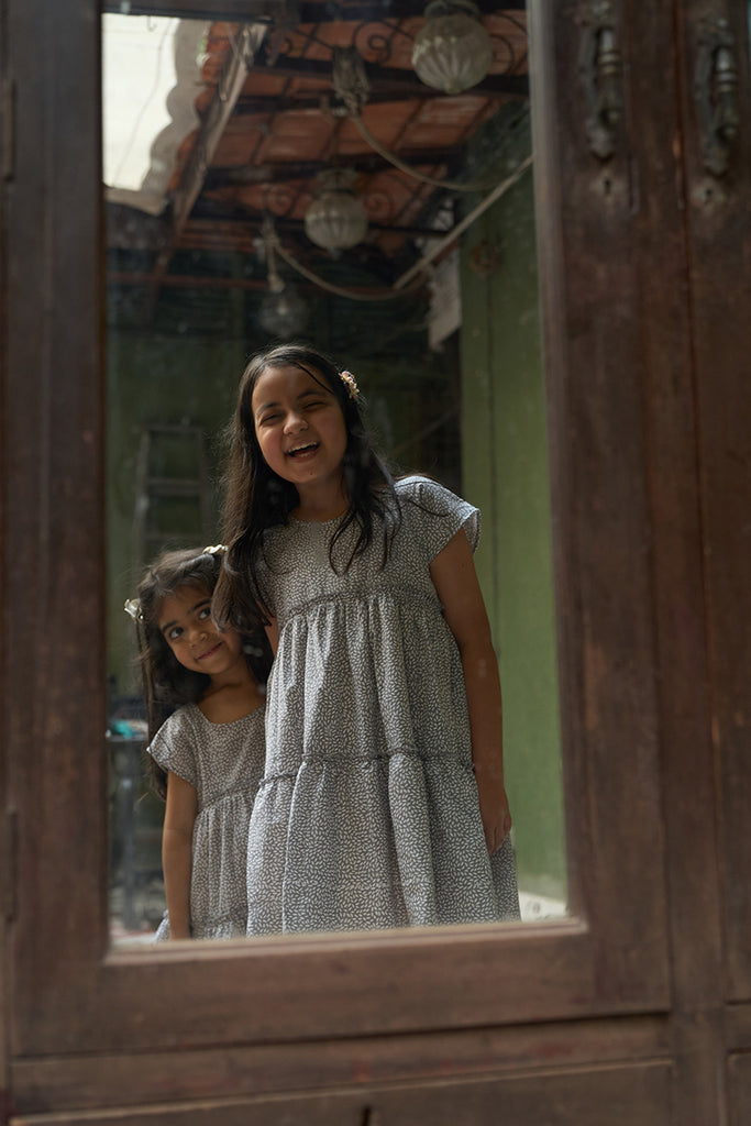 baby-girls-looking-at-themselves-in-the-mirror-dressed-in-matching-clothes-wearing-lovetheworldtodays-tiered-dress-in-grey-hand-block-print