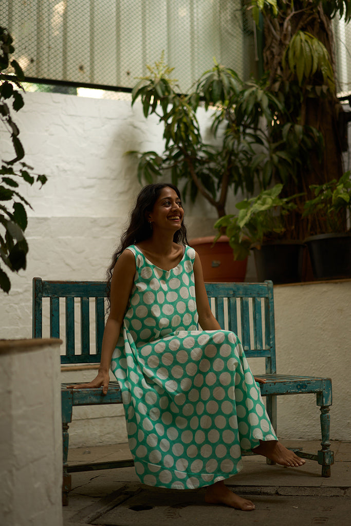 woman-sitting-on-a-blue-vintage-chair-in-lovetheworldtodays-womens-sleeveless-summer-flared-dress-in-blue-polka-handblock-print-purecotton-made-in-jaipur